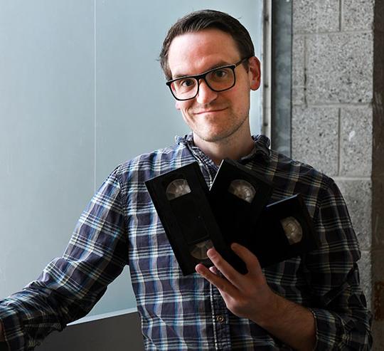 headshot of man with glasses, holding VHS tapes